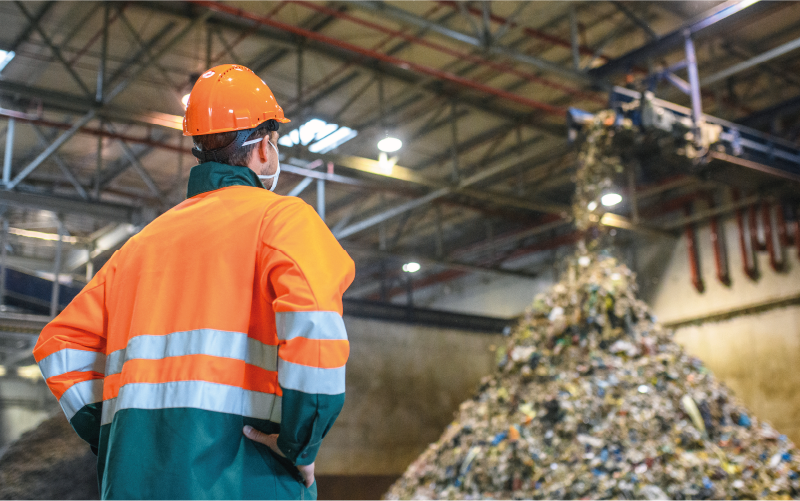 Photograph of a workman facing away from camera and looking at a large pile of rubbish
