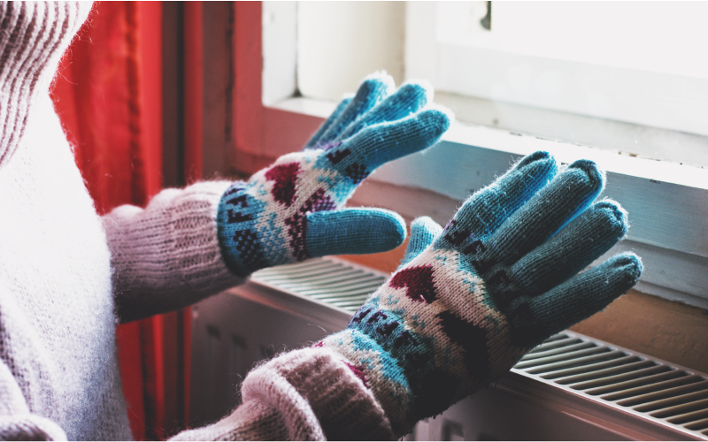 A person wearing gloves with their hands over a radiator