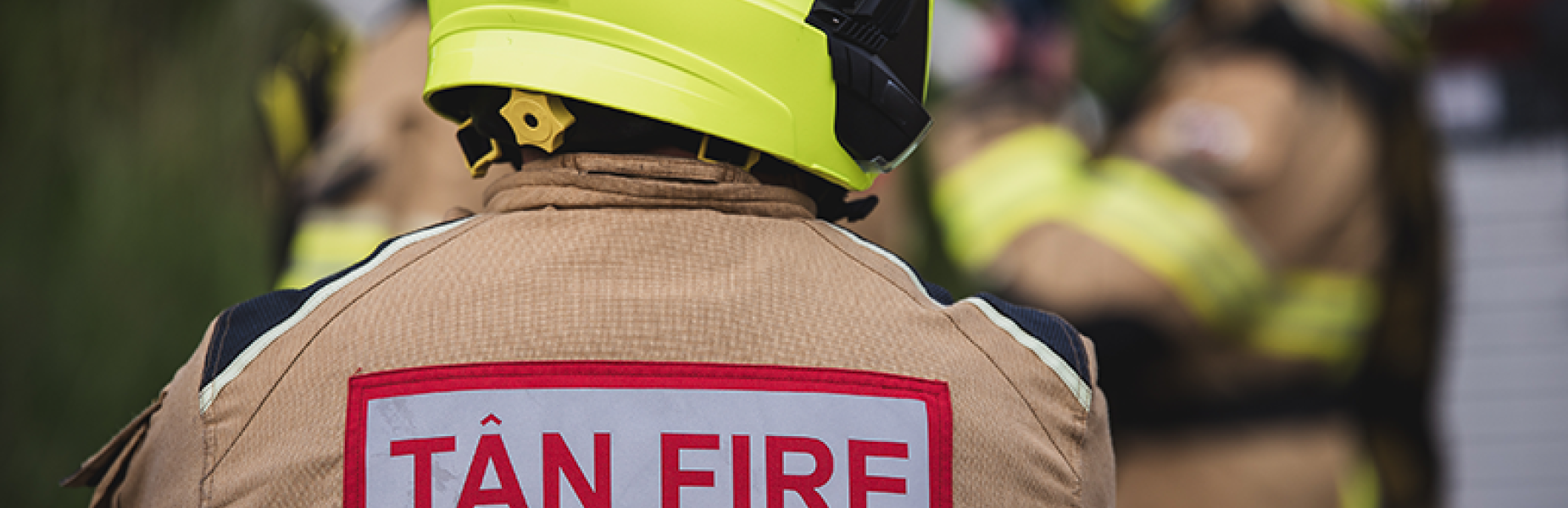 The back of a fire person wearing a helmet and a jacket with the wording  Tan/ fire on it