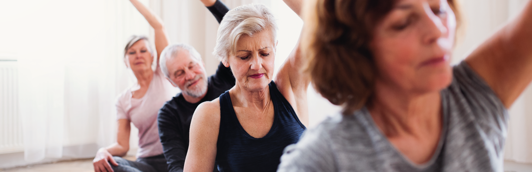 Group of people at an exercise class with their hands curving above their heads in a yoga position