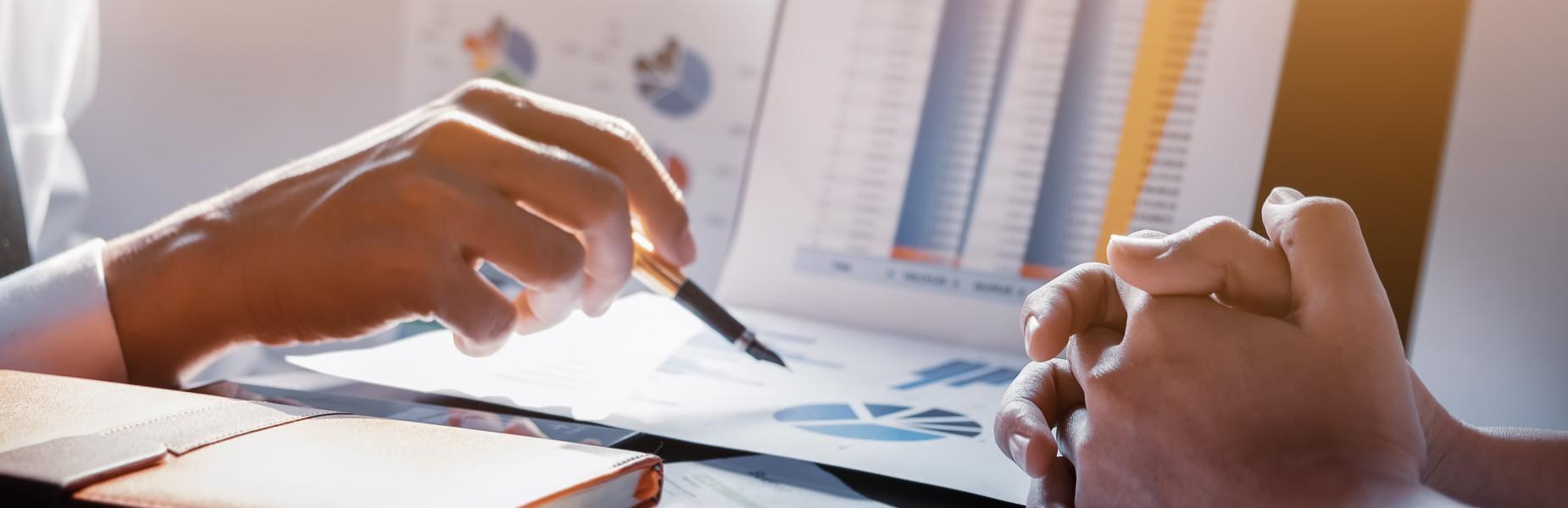 Hands discussing charts and graphs on a desk