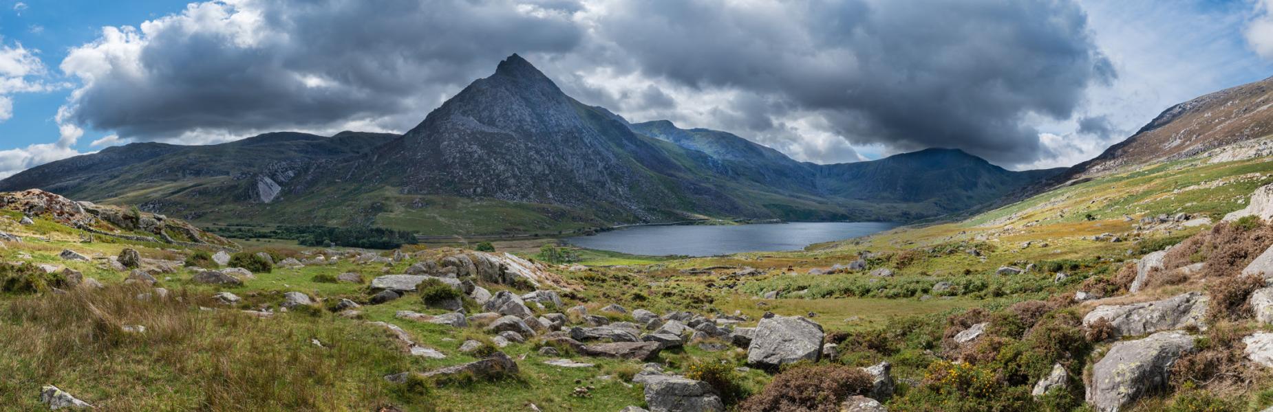 Mountain peak overlooking a lake beneath dramatic clouds in a rugged Welsh landscape.