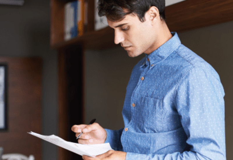 Photograph of a young man in a blue shirt holding pen and paper