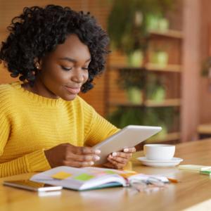 Woman sitting at a table reading newsletter on her tablet